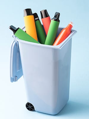 Several disposable vapes are lying in an open trash can.